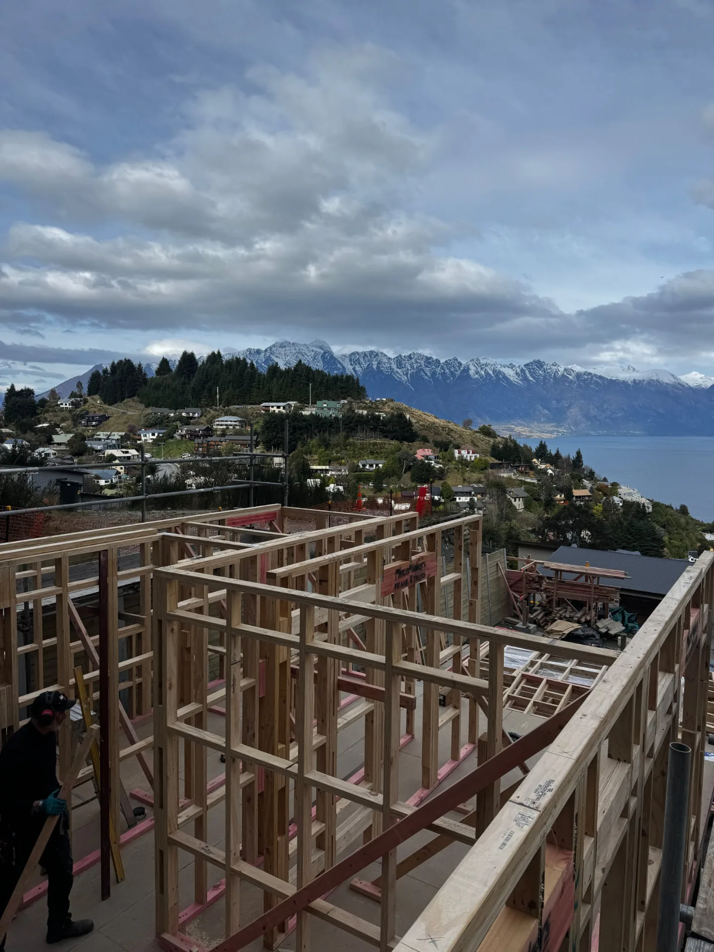 Builder beside Te Tihi Villas timber wall framing with snow on the Remarkables beyond