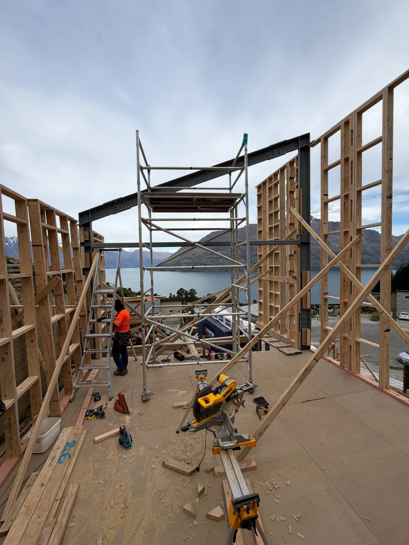 Builder working inside Te Tihi Villas timber framing, with a steel portal frame and views over Lake Wakatipu to the mountains